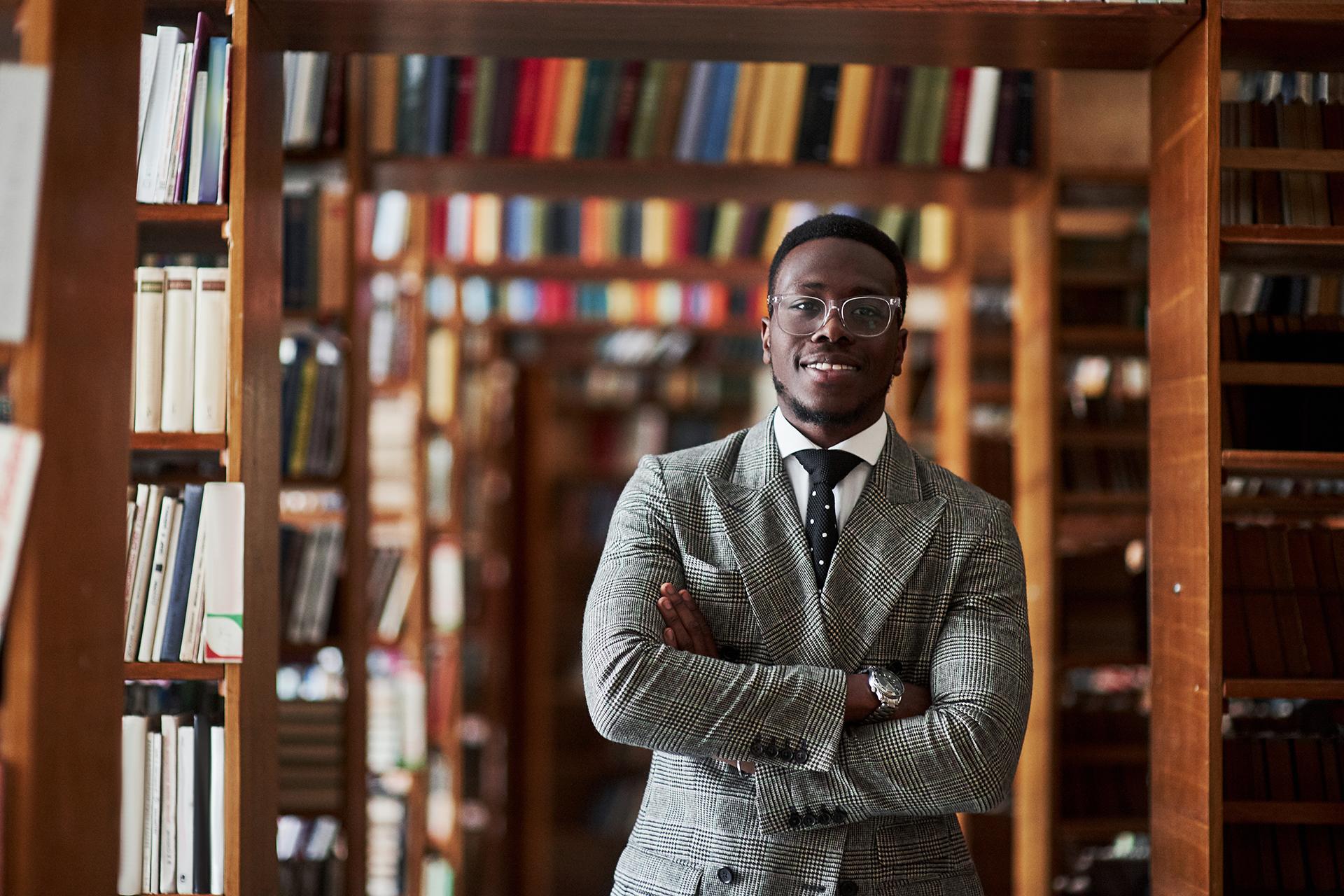 An African American man in a business suit standing in a library in the reading room man in a business suit standing in a library in the reading room.